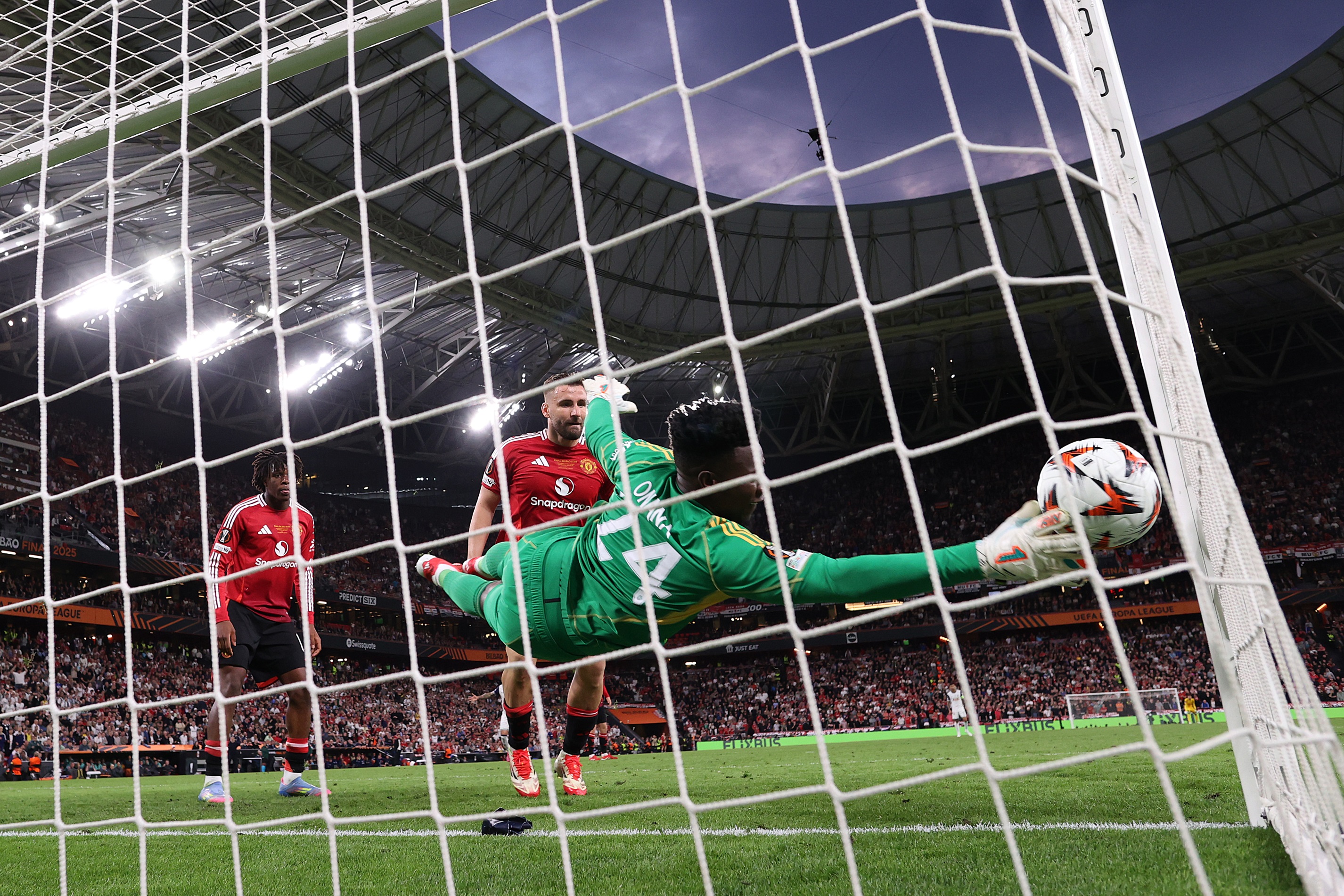 Andre Onana dives to his right with his fingertips touching a ball in mid-flight.