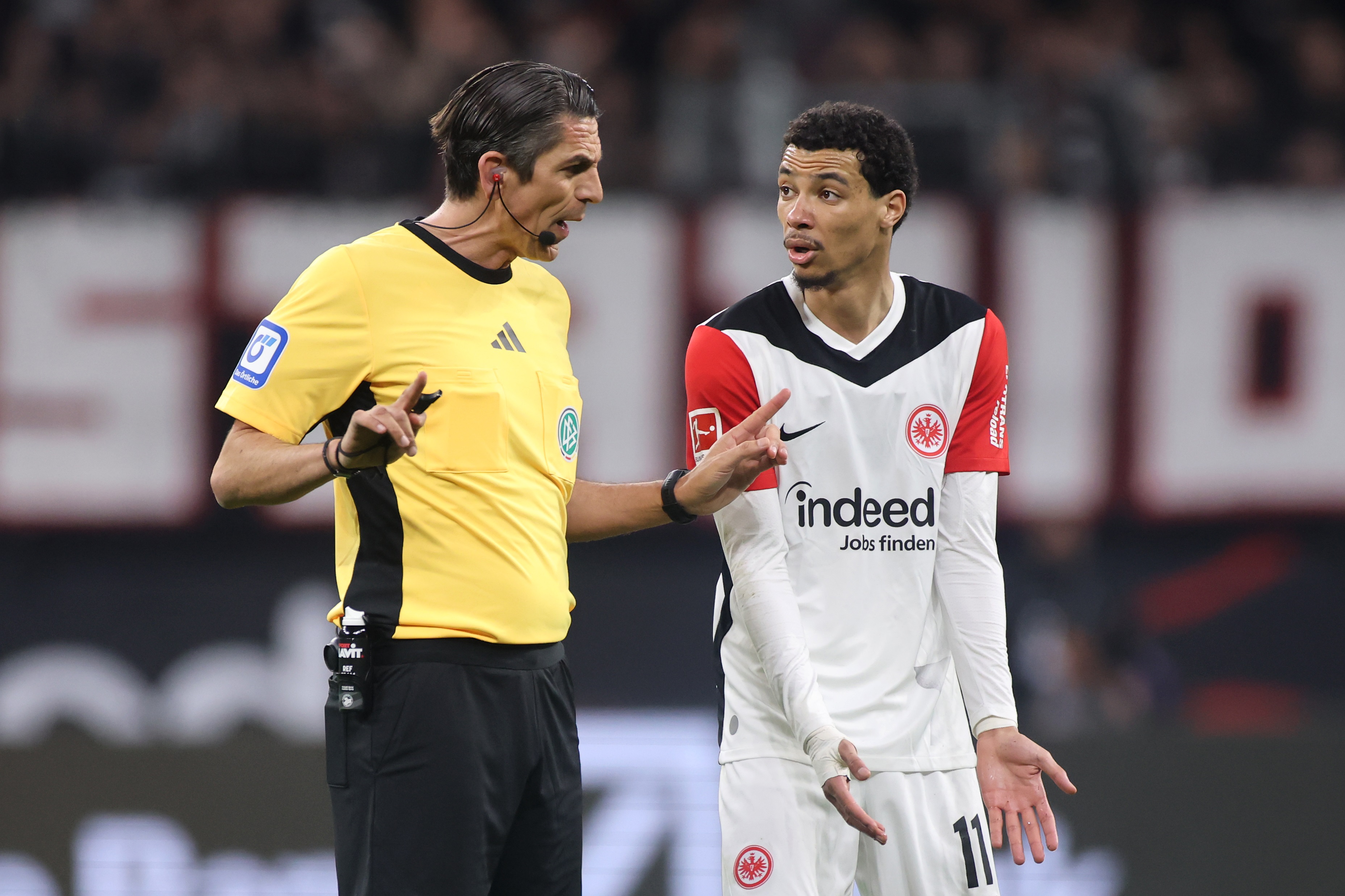 Hugo Ekitike gestures at the ground with both hands in conversation with referee.