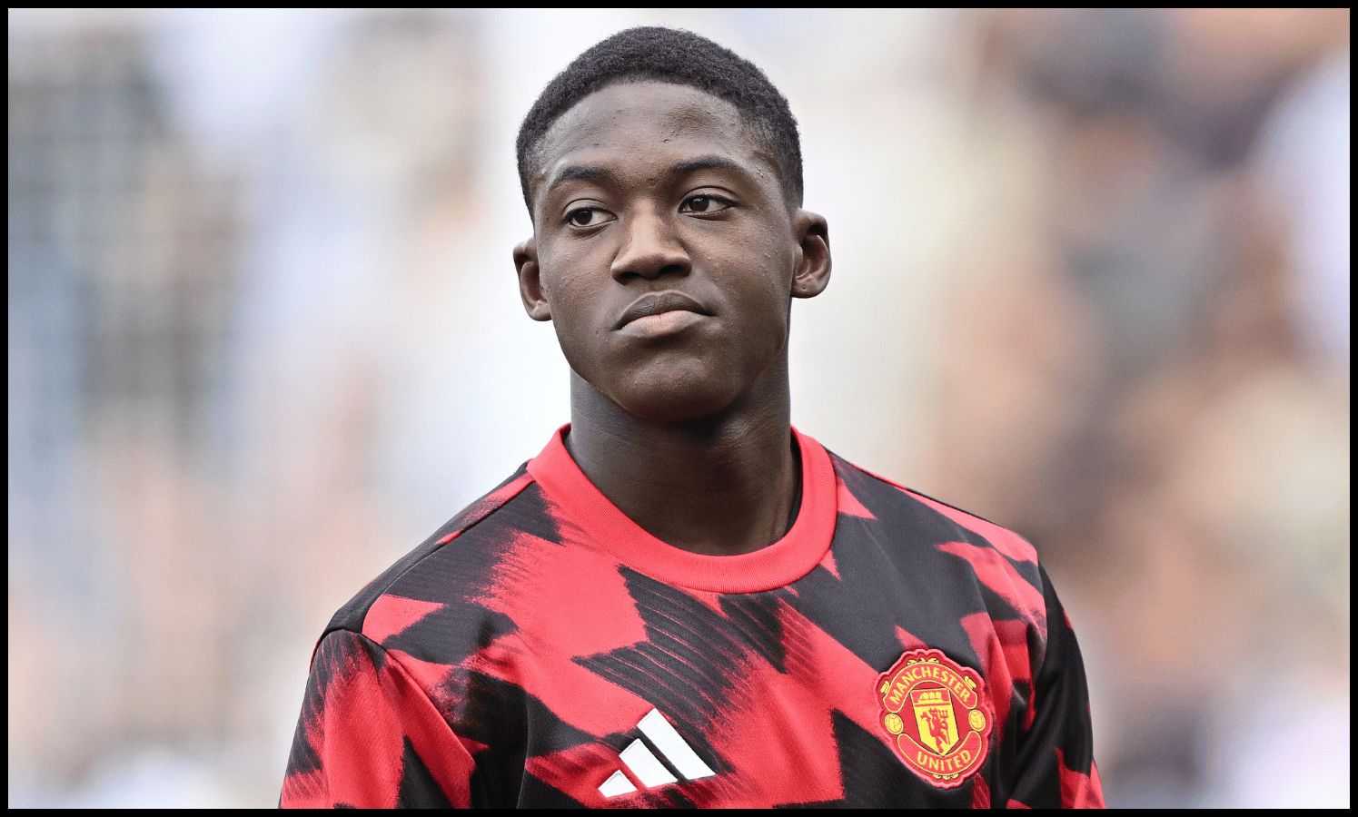 Kobbie Mainoo looks on while warming up for Man United.